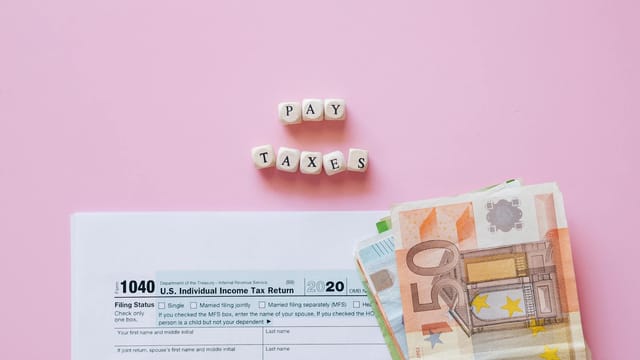 Top view of tax form, euro banknotes, and 'Pay Taxes' letter blocks on pink background.