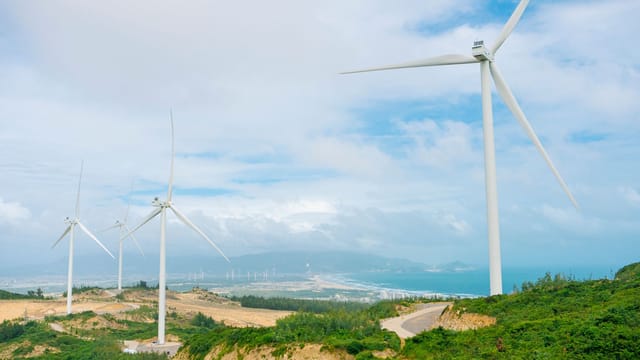 Aerial view of wind turbines on a hilly landscape under a clear blue sky, promoting renewable energy.
