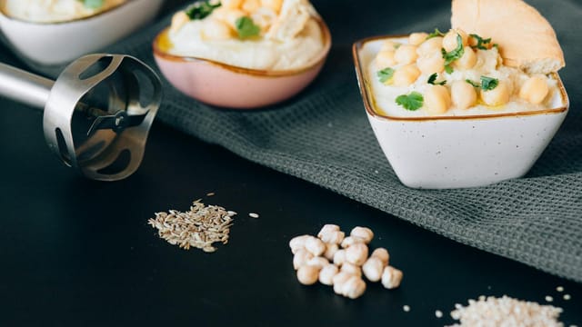 Delicious creamy hummus garnished with chickpeas and herbs, presented in a modern kitchen setting.