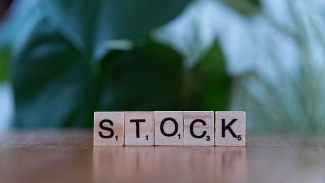 Close-up of wooden letter blocks spelling 'STOCK' on a table against a blurred green background.