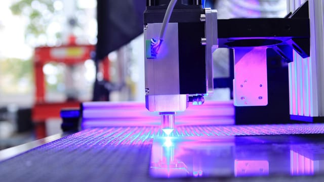 Close-up of a laser engraving machine working indoors with blue light reflection.