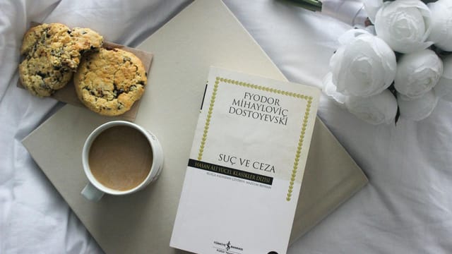 Top view of a book, coffee, and cookies on a bed with white roses.