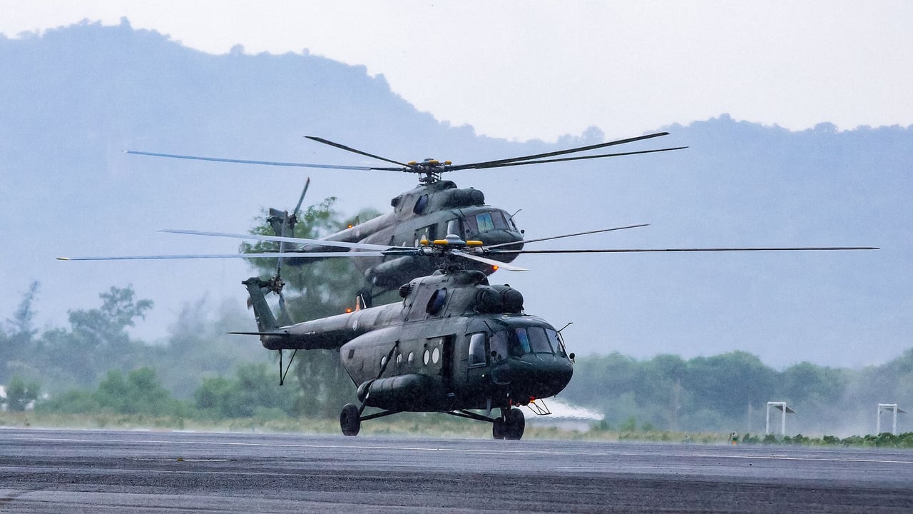 Modern armed military helicopters landing on asphalt ground against rocky hills in countryside on daytime