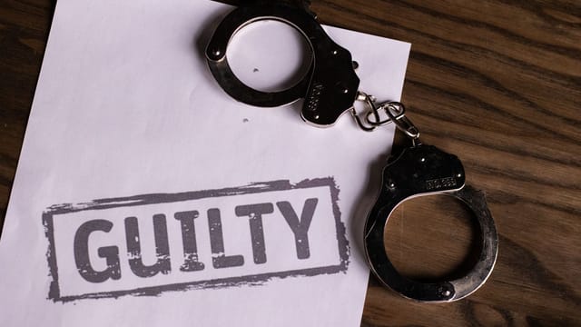 Top view of handcuffs on paper with 'GUILTY' text, symbolizing a verdict or crime.