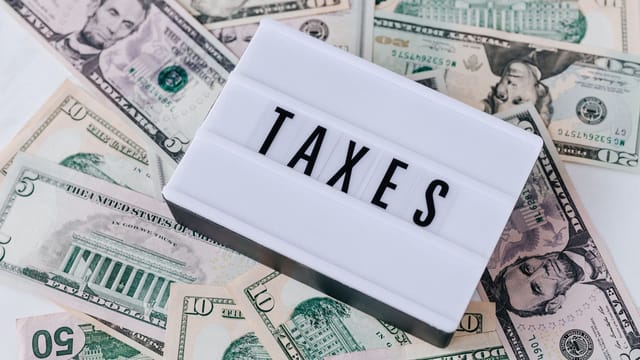 From above of white retro lightbox with TAXES inscription placed on pile of USA dollar bills on white surface