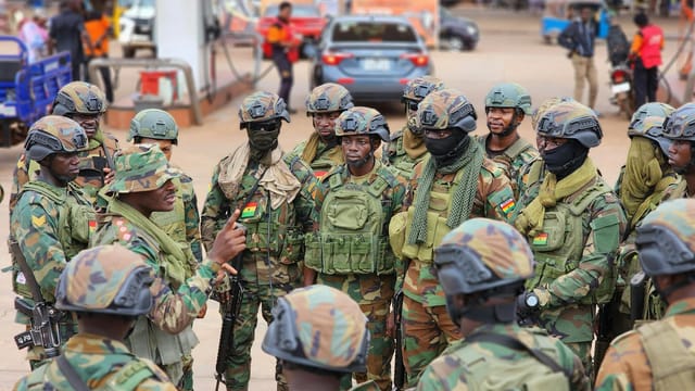 Military personnel in camouflage uniforms engaged in a briefing in an urban environment.