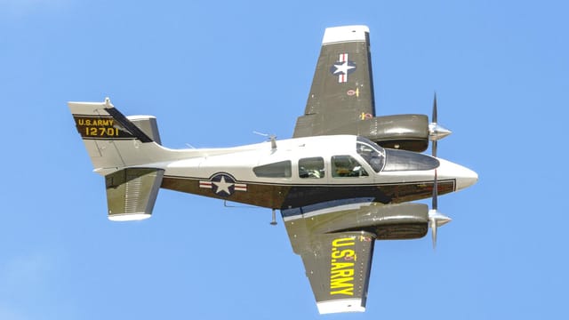 Beechcraft E55 Baron aircraft flying under clear blue skies during daytime.