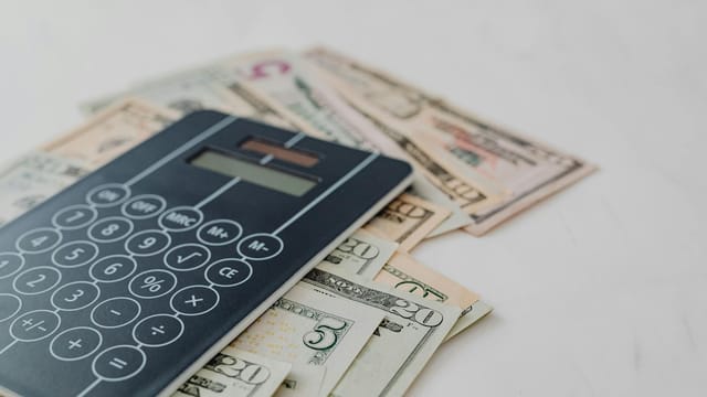 A close-up of a calculator and US dollar banknotes, symbolizing financial calculation and budgeting.