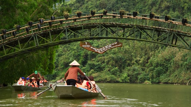 Group boating on a tranquil river under a rustic bridge amidst lush greenery.