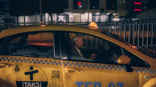 A yellow taxi navigating through an urban environment on a rainy night.
