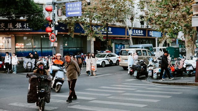 Street life in Nanjing, China with people, scooters, and autumn foliage on a busy corner.