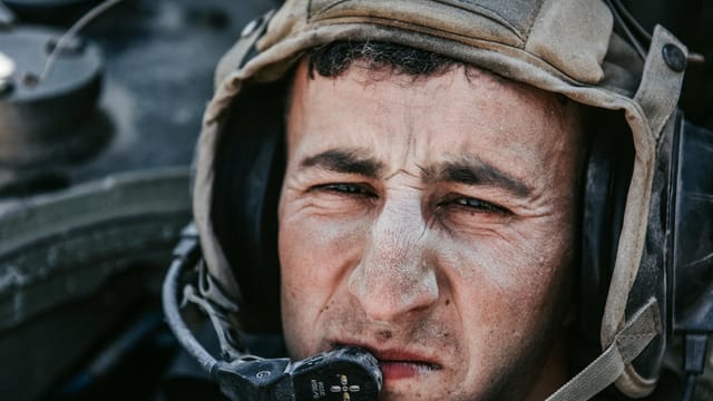 Intense close-up of a soldier wearing a military helmet and communication headset, focused and serious.