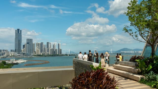 Scenic view of Shenzhen Bay with people enjoying the skyline from a green terrace.