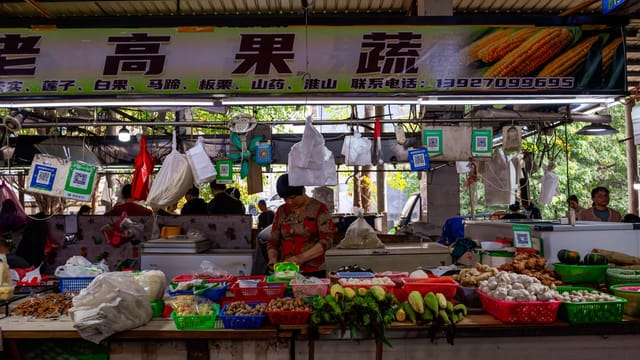 Bustling Asian market stall with vendor selling fresh produce and vegetables.