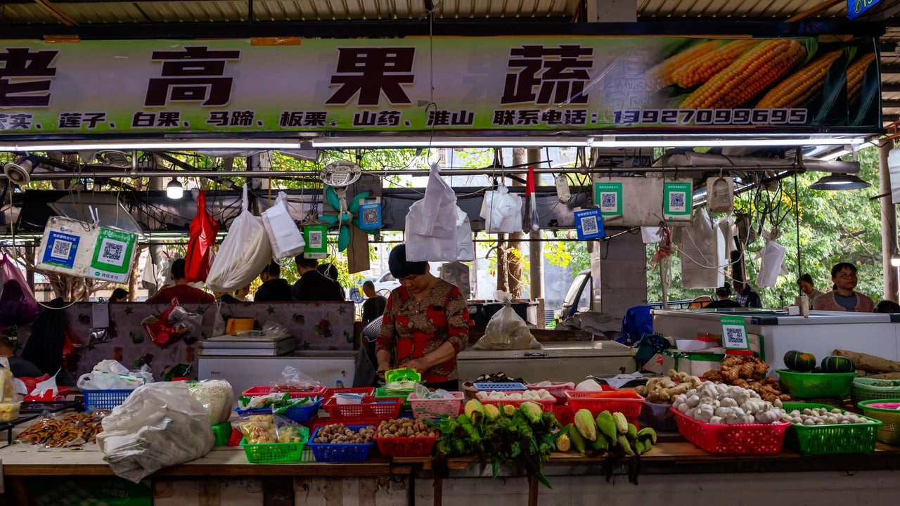 Bustling Asian market stall with vendor selling fresh produce and vegetables.