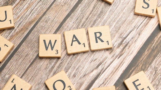 Close-up of wooden scrabble tiles spelling 'WAR' on a wooden background.