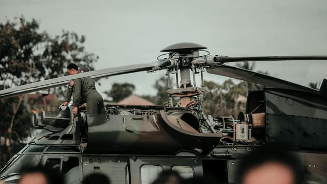 A military helicopter with crew performing maintenance during daytime outdoors.