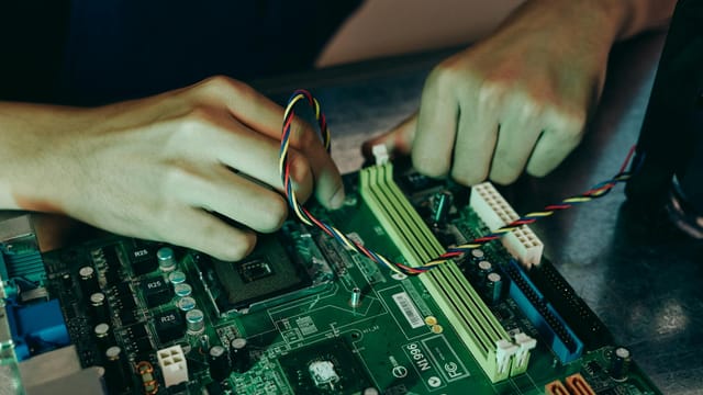 Person assembling computer motherboard with colorful wires, showcasing technology and engineering.