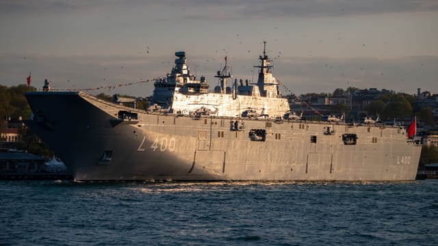 Military battleship L400 moored near a coastal town at sunset, showcasing its grandeur.