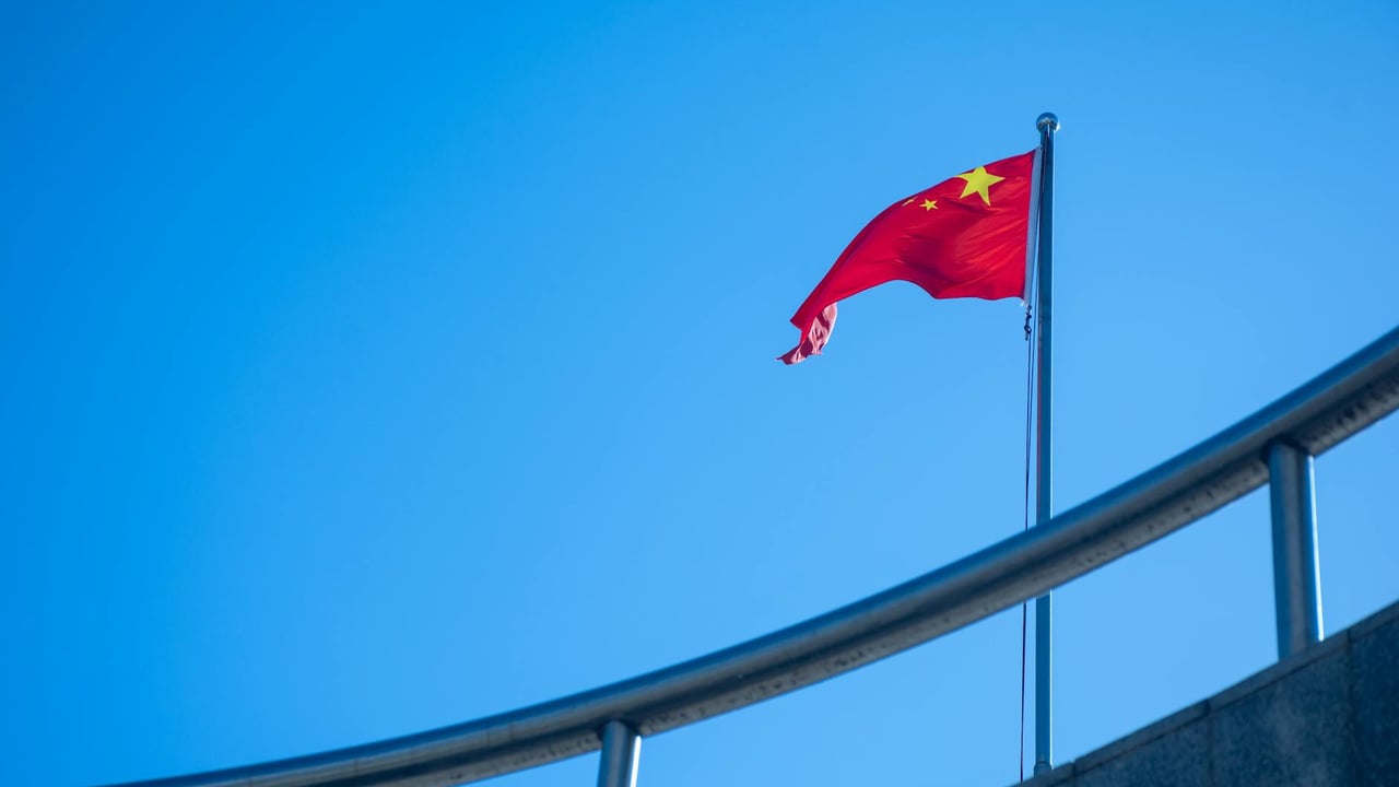 The Chinese national flag waving against a clear blue sky, symbolizing patriotism.
