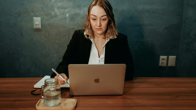 A focused businesswoman working on a laptop in a stylish office setting. Professional and determined demeanor.