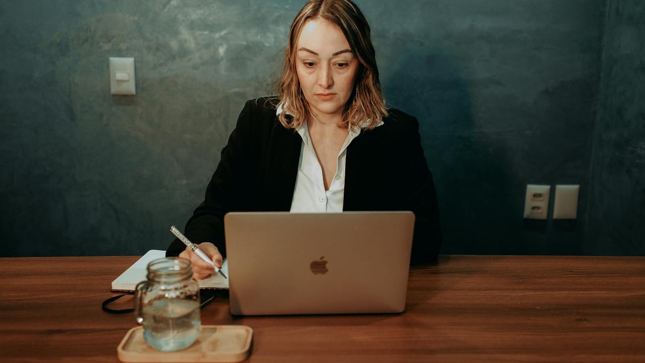 A focused businesswoman working on a laptop in a stylish office setting. Professional and determined demeanor.