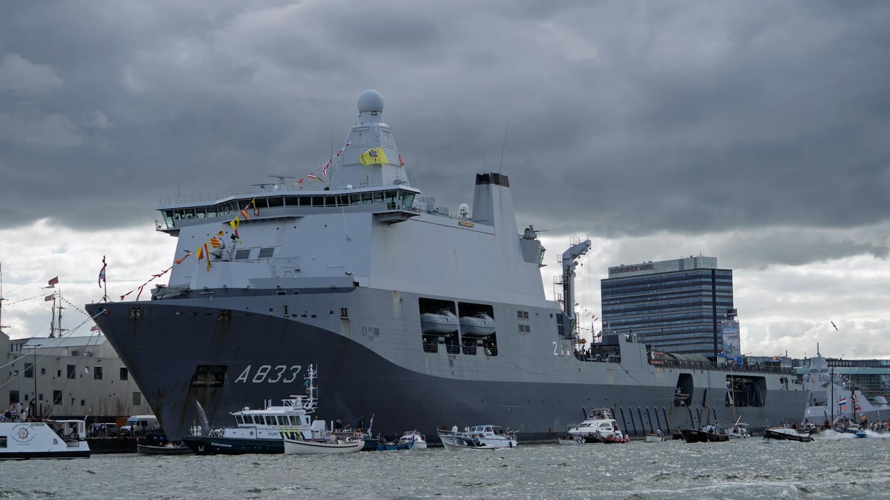 A large navy ship A833 docked in a busy harbor with smaller boats and cloudy skies.