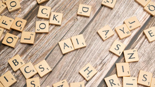 Wooden letter tiles scattered on a textured surface, spelling 'AI'.