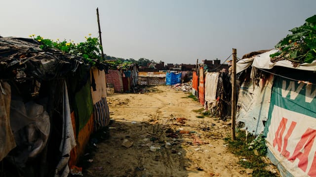 A dusty rural pathway flanked by makeshift shelters covered in tarps and signs.