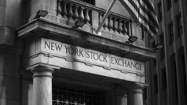 Black and white photo of the New York Stock Exchange facade with USA flag.