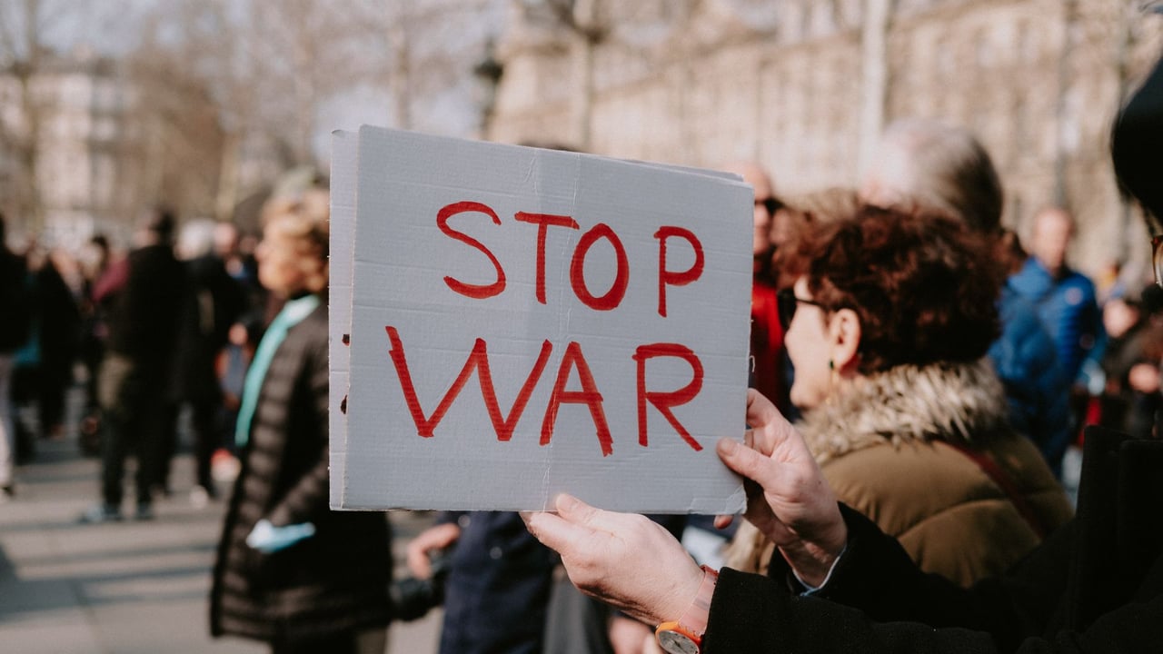 Crowd of people in a peaceful protest holding a 'Stop War' sign outdoors.