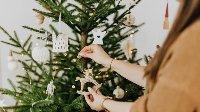 Woman places ornaments on a Christmas tree, enhancing festive atmosphere indoors.