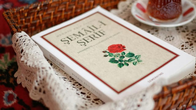 An artistic setup with a Turkish book in a wicker basket and a cup of tea on a lace doily.