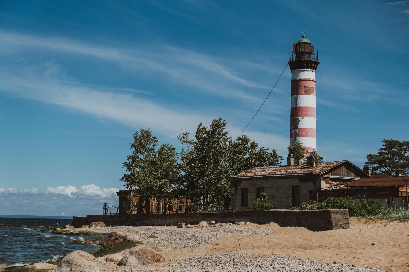 A scenic view of the iconic Shepelyovsky Lighthouse on a sunny day by the rocky shore.