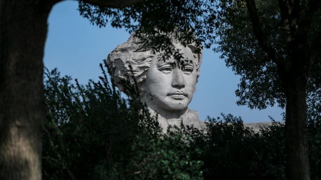 A statue of Mao Zedong emerges through lush greenery, captured in a tranquil outdoor setting.