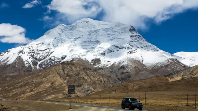 Stunning view of a snowy mountain in Ngari, with a car on a scenic road below.
