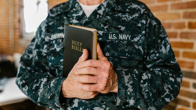 A U.S. Navy sailor in uniform holding a Holy Bible, symbolizing faith and service.