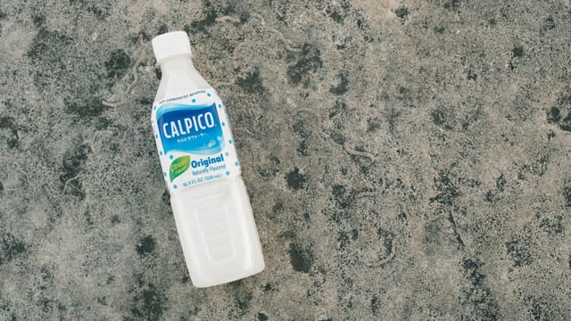 A bottle of Calpico original flavored beverage placed on a textured concrete surface.