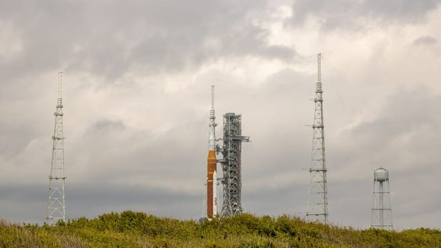 NASA rocket on launch pad surrounded by antennas against a cloudy sky.