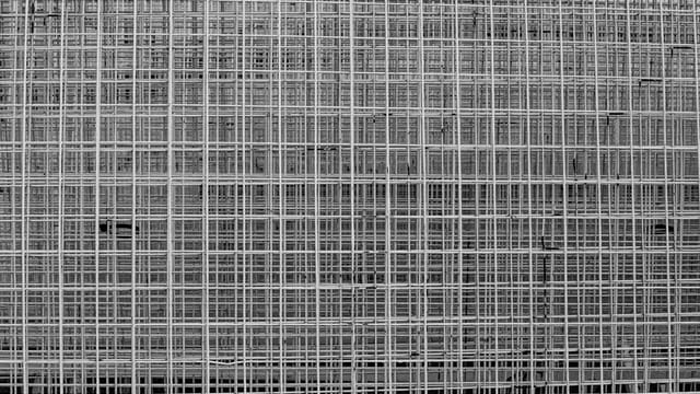 A detailed black and white photograph of a geometric wire grid pattern creating urban texture.