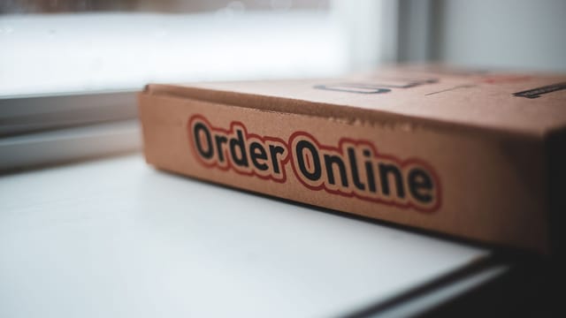 Soft focus of cardboard box of delivery pizza online service placed on white windowsill in daylight
