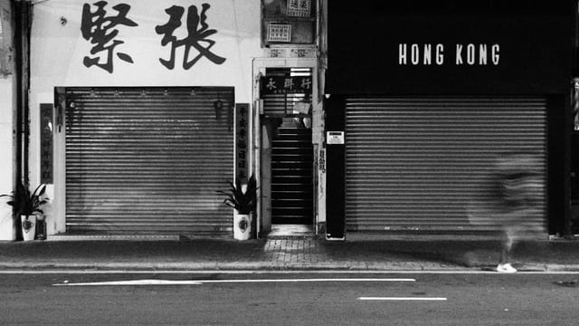 Blurred figure in a Hong Kong street with closed shutters and signage.