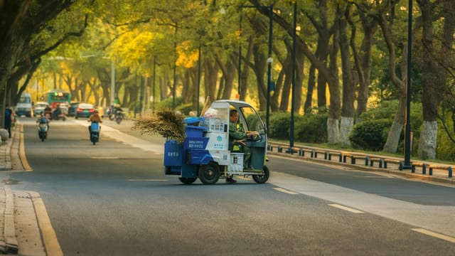 Street cleaning vehicle on tree-lined avenue in Suzhou, China during daytime.