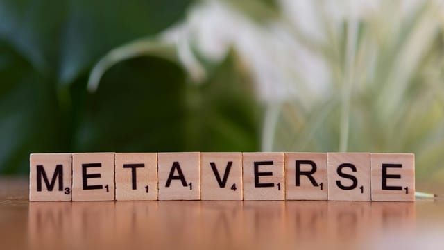 Scrabble letters spelling 'Metaverse' on a wooden surface with a blurred nature background.