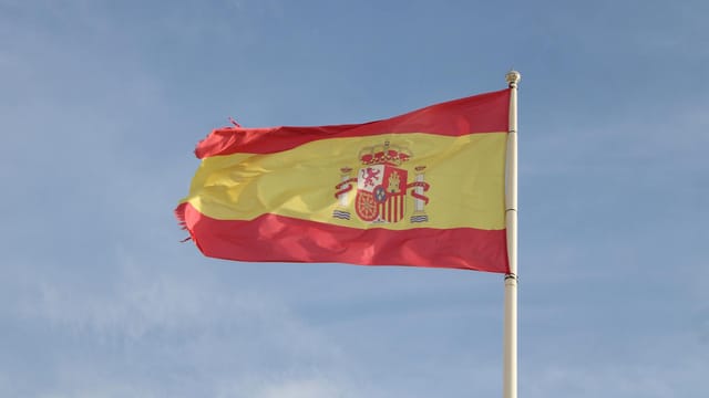 Spanish flag flying high on a flagpole against a clear sky in Andalucía, Spain.