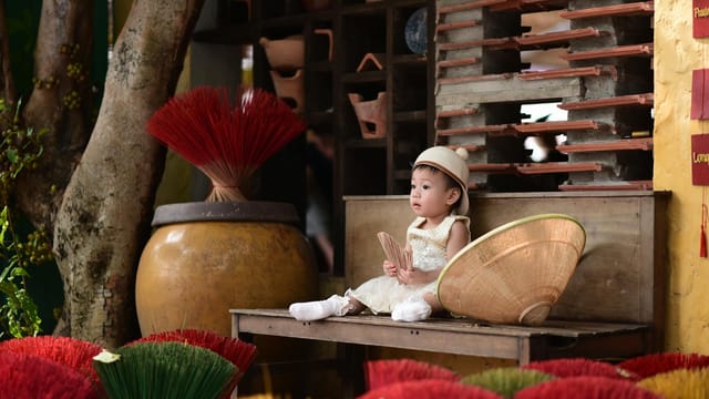 Adorable child with traditional Vietnamese hat and incense sticks, capturing cultural charm.