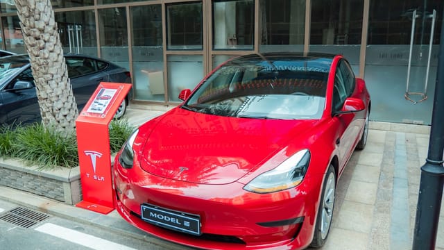 Shiny red Tesla Model 3 parked on sidewalk with reflections on windshield.