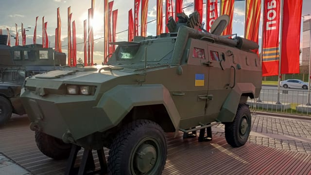 An armored military vehicle showcased outside with flags and sunlight in Moscow.