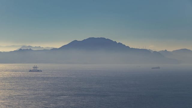 Serene view of the sea and distant mountains near Gibraltar during the day, with ships visible on the horizon.