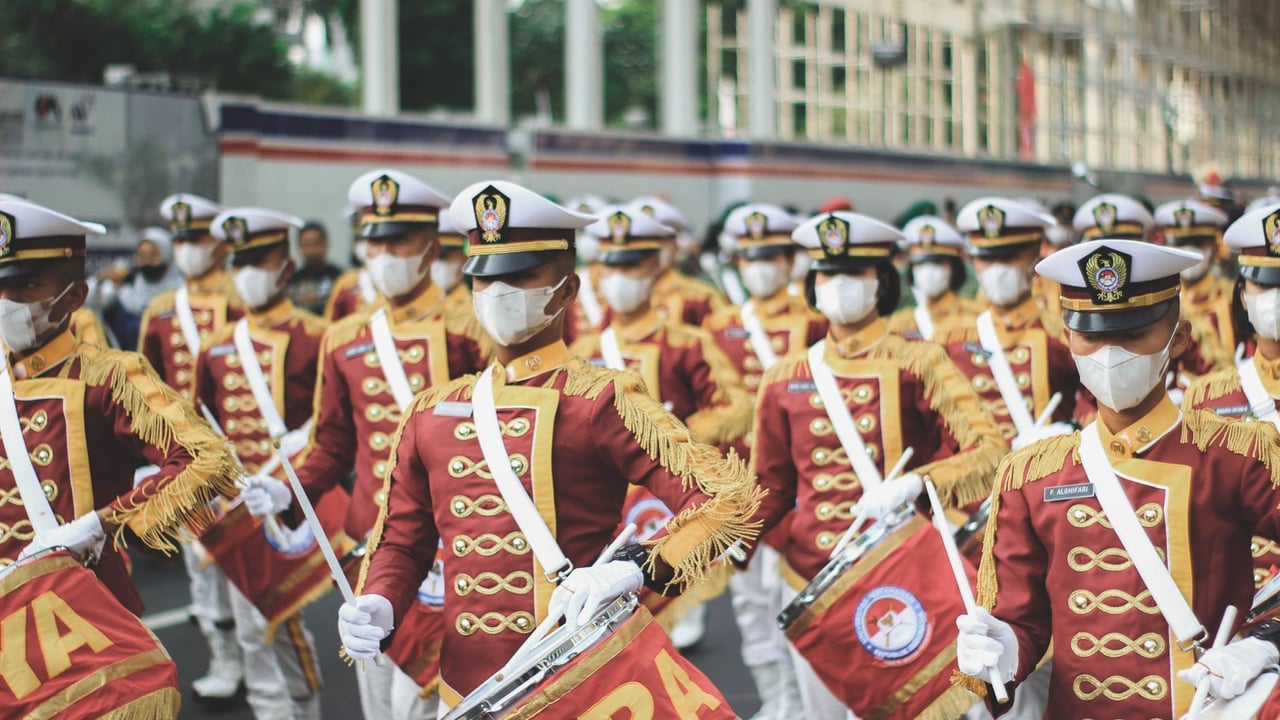 Military band performing in a street parade with colorful uniforms and drums.